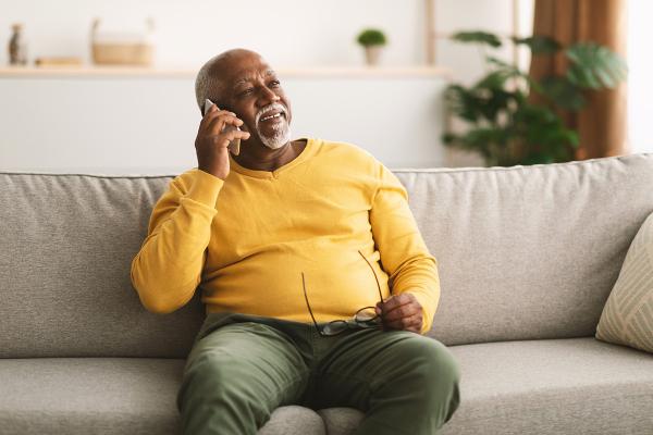 A man holding up a phone to his ear, sitting on a couch